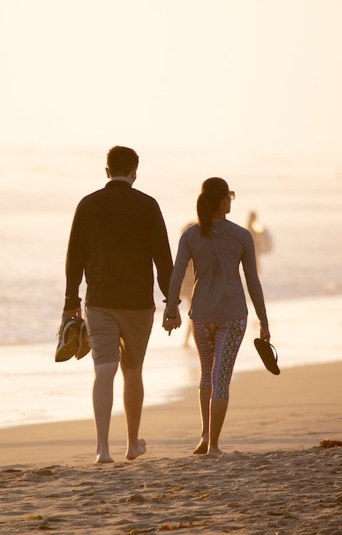 two couples walking on the shore with footwear removed