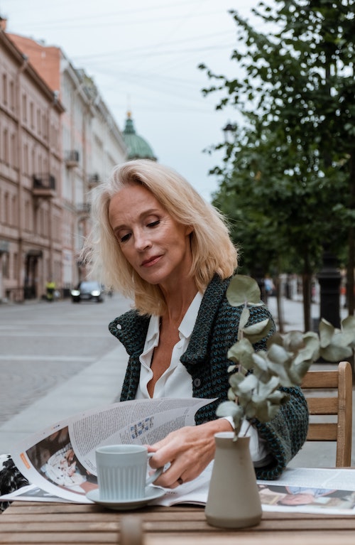 a gorgeous older woman reading a newspaper in an outside the cafe setting